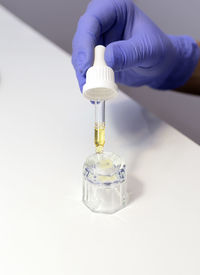 Closeup nail technician holds pipette with natural oil for cuticle, fingernails above glass cup. eco