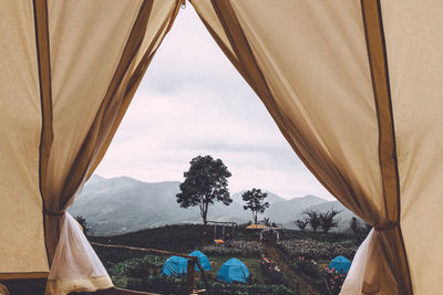 View of tent against cloudy sky seen through window