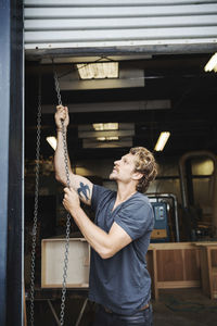 Carpenter pulling shutter at entrance of workshop