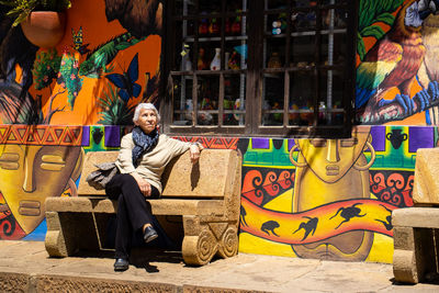 Senior woman tourist sitting on a bench at the beautiful streets of the city of raquira. 