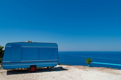Blue caravan parked on shore against clear sky