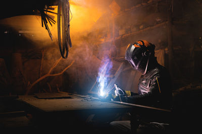 Village workshop, welding in an old garage. an unrecognizable man repairs a metal part wearing