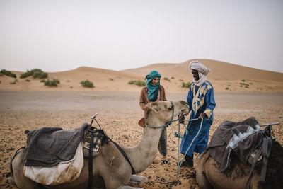 Tourist with guide touching camel at desert 