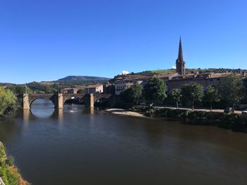 Arch bridge over river amidst buildings against clear blue sky