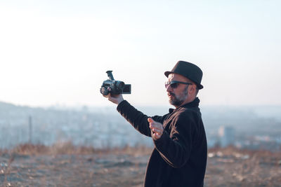 Man holding camera while standing on land against sky