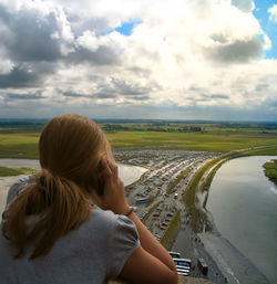 Rear view of girl sitting on lake against sky