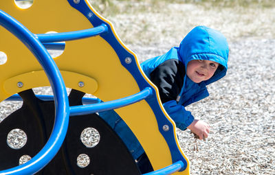 Little boy in blue coat playing hide and seek on the playground