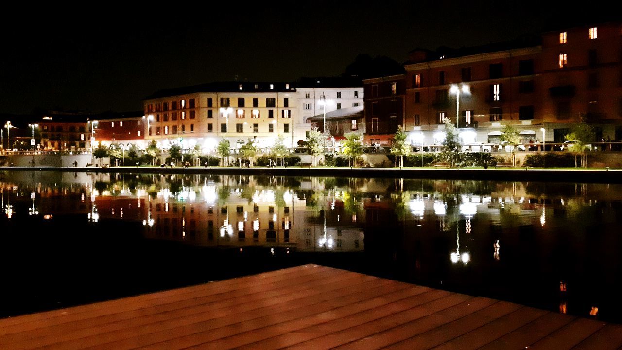 ILLUMINATED BUILDINGS BY LAKE IN CITY AT NIGHT