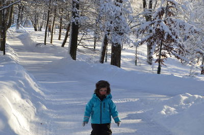 Cute boy standing on snow covered field against trees