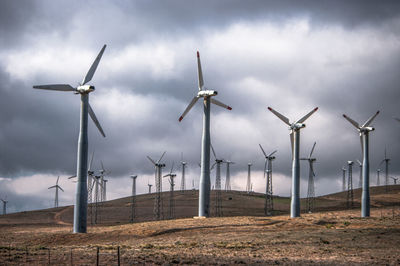 Windmills on field against cloudy sky