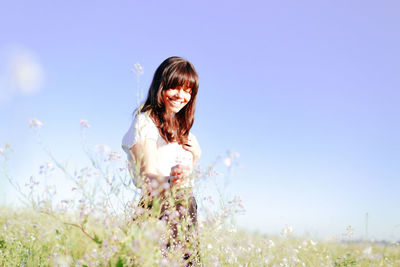 Portrait of young woman standing on field against clear sky