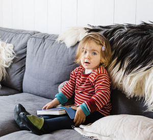 Portrait of girl reading book while sitting on sofa at home