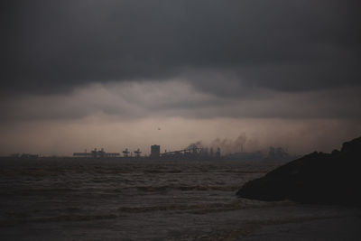Silhouette buildings by sea against sky at sunset