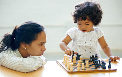 Cute girl playing chess with mother