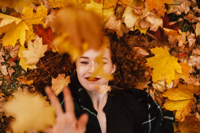 Young redhead woman lying on field with orange dry leaves in autumn