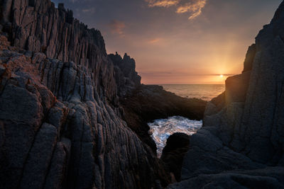 Rock formation on beach against sky during sunset