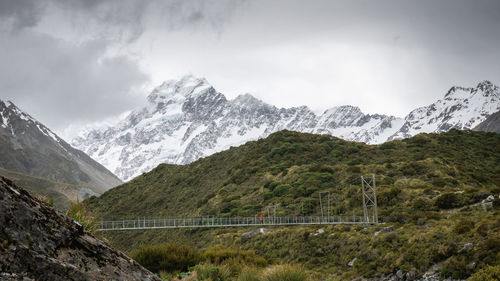 Mountain and man crossing swing bridge , shot at aoraki mt cook national park, new zealand