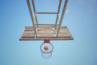 Low angle view of basketball falling into hoop against blue sky