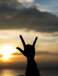 Close-up of silhouette hand gesturing against sky during sunset