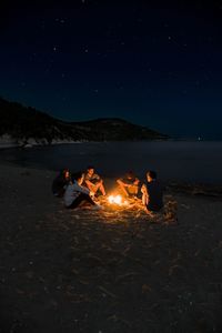 People sitting on bonfire against sky at night