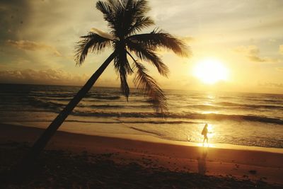 Woman walking at beach against sky during sunset