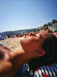 Close-up of woman napping at beach against clear sky during sunny day