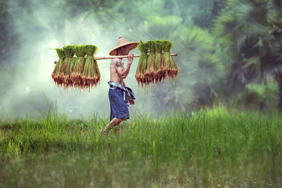 Man working in basket on field against sky