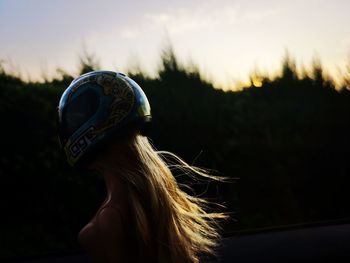 Woman wearing helmet against sky during sunset