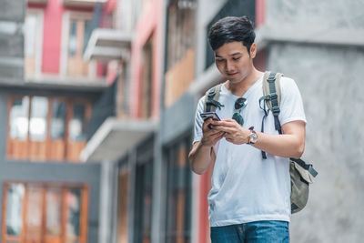 Young man using mobile phone standing against building