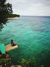 High angle view of man sitting on diving platform against turquoise sea