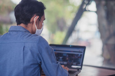 Man wearing mask using laptop at desk