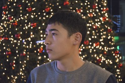 Thoughtful teenage boy against illuminated christmas tree at night