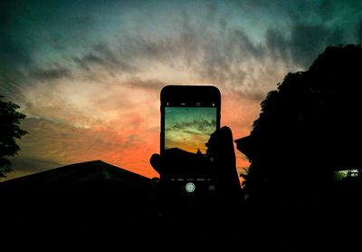 Silhouette man using smart phone against sky at sunset