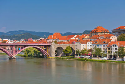 Arch bridge over river by buildings against clear blue sky