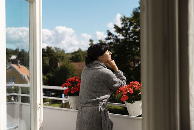 Woman with hand on chin enjoying sunlight while leaning on railing in balcony