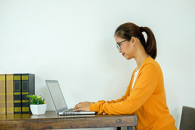 Woman looking at smart phone while standing on table against wall