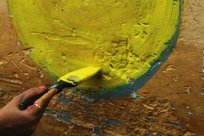 Midsection of person holding umbrella against yellow wall