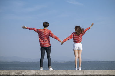 Couple standing together on retaining wall against sea