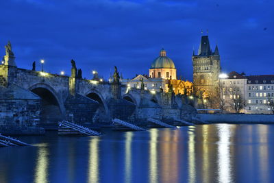 Illuminated bridge over river by buildings against sky in city