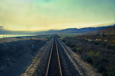 Empty road amidst field leading towards mountains against sky