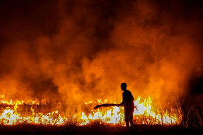 Silhouette man standing by fire at night