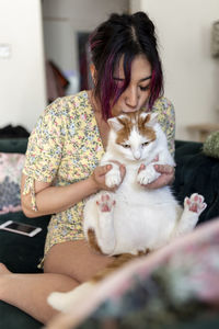 Young woman kissing and playing with cat at home