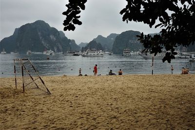 People on beach by mountains against sky