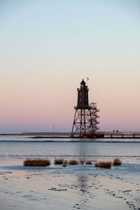 Lighthouse by sea against clear sky during sunset