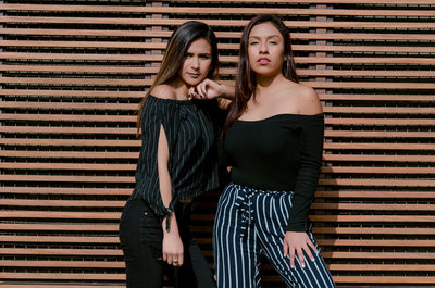 Portrait of fashionable women standing against blinds