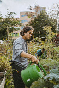 Young male environmentalist watering plants in community garden