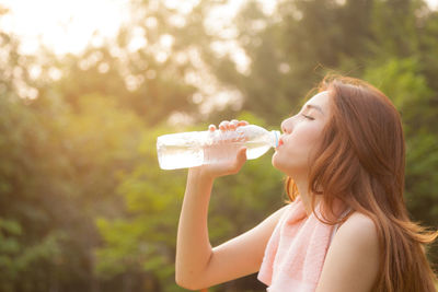 Woman drinking water from bottle against trees