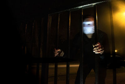 Man wearing mask holding gate outdoors at night