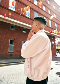 Side view of young man looking away against building