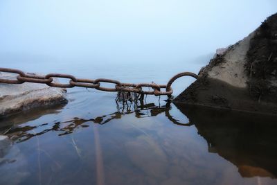 Rusty metal chain on lake against sky